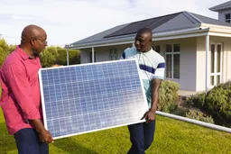 african american senior father and son carrying solar panel